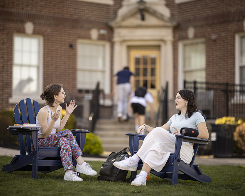 Two girls relaxing in chairs outside of a dorm